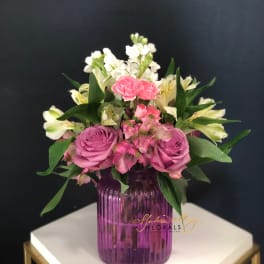 Pink and white flower arrangement in a purple glass vase