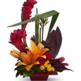 Tropical floral arrangement with orange lilies and red blooms in a red container
