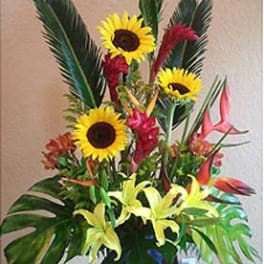Tall tropical arrangement with yellow sunflowers, lilies, and red-orange flowers in a dark vase