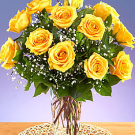Arrangement of yellow roses with white filler flowers in a clear glass vase