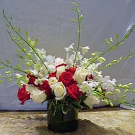 Red and white rose arrangement with white orchids and green sprays in a glass cylinder vase