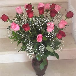 Tall arrangement of red and pink roses with white filler flowers in a dark vase