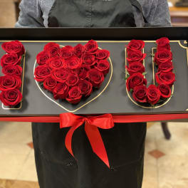 Red roses arranged to spell I love you in a black gift box