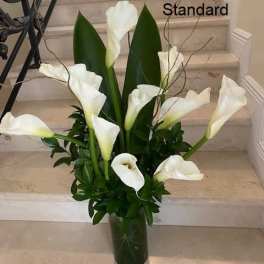 Tall arrangement of white calla lilies in a clear glass vase on stone steps