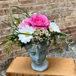 Pink rose arrangement in a blue face-shaped vase with white daisies