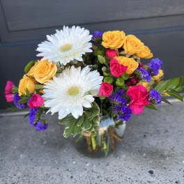 Mixed bouquet of white daisies, yellow roses, and pink blooms in a glass vase