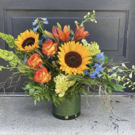 Mixed bouquet with sunflowers, roses, lilies, and blue flowers in a green vase