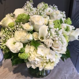 White floral arrangement with roses, calla lilies, and hydrangeas in a glass vase