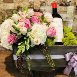 Pink and white floral arrangement in a wooden box with a wine bottle