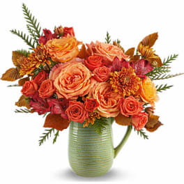 Orange and coral roses with mums in a green ceramic pitcher