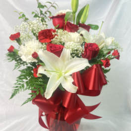 Red and white flower arrangement in a glass vase with a red ribbon