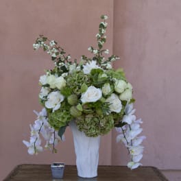 White and green floral arrangement in a tall white vase with trailing orchids