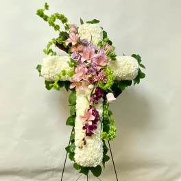 White floral cross on an easel with pink and purple flowers