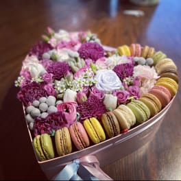 Heart-shaped box of pink and white flowers with colorful macarons around the edge