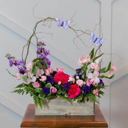 Pink and purple floral arrangement in a wooden box with butterfly picks