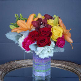 Mixed bouquet of roses, lilies, orchids, and carnations in a glass vase