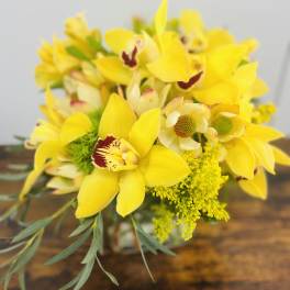 Yellow orchid bouquet with green filler in a glass vase
