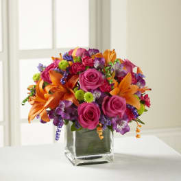 Bright mixed bouquet of roses, lilies, and purple blooms in a glass vase