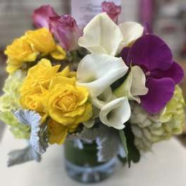 Bouquet of yellow roses, white calla lilies, and purple orchids in a glass vase