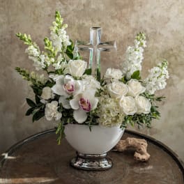 White floral arrangement in a white vase with a clear cross centerpiece