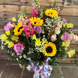 Bouquet of sunflowers, pink roses, and mixed blooms in a glass vase