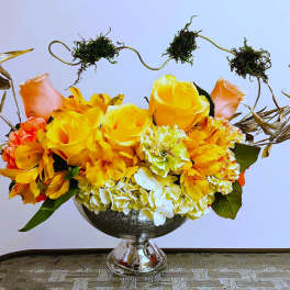 Yellow and orange flower arrangement in a silver pedestal vase