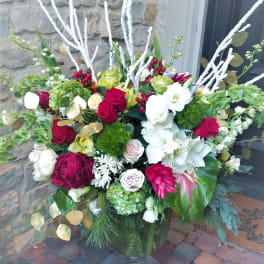 Large mixed floral arrangement in a glass vase with red, white, and green blooms
