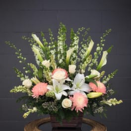Large floral arrangement with white lilies, roses, and pink mums in a wooden container