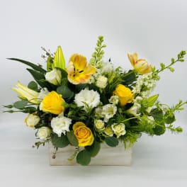 Low rectangular arrangement of yellow and white flowers in a whitewashed wooden box