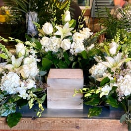 White floral arrangement with lilies and roses around a wooden cube