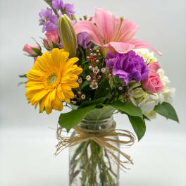 Mixed bouquet in a glass jar vase with pink, purple, yellow, and white blooms