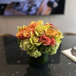 Orange roses and yellow orchids in a green vase