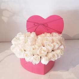 White roses arranged in a pink heart-shaped box
