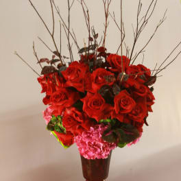 Red roses and pink hydrangeas in a red pedestal vase with tall branches