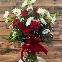 Red roses and white daisies in a glass vase with a red ribbon