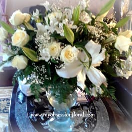 Large white floral arrangement with roses and lilies in a glass vase
