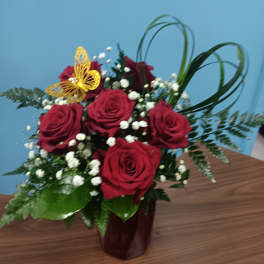 Red roses arranged in a dark vase with baby's breath and greenery