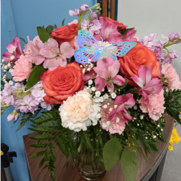 Pink and orange flower bouquet in a glass vase with a blue butterfly pick