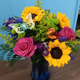 Bouquet of sunflowers, pink roses, and purple flowers in a blue vase