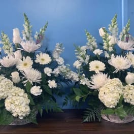 Two white floral arrangements in baskets with daisies and hydrangeas