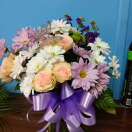 Mixed bouquet of pastel roses and daisies in a glass vase with a purple ribbon