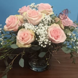 Pink roses and baby's breath in a glass vase with a butterfly decoration
