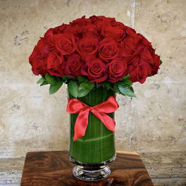Red roses arranged in a tall glass vase with a red ribbon