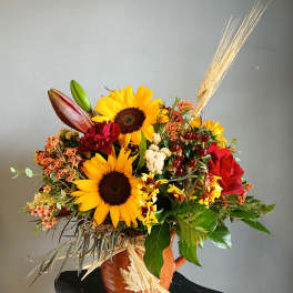 Sunflower arrangement in a ceramic vase with red roses and wheat accents