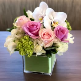 Pink and white roses with white orchids in a green square vase