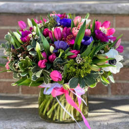Mixed bouquet of pink, purple, white, and blue flowers in a glass vase