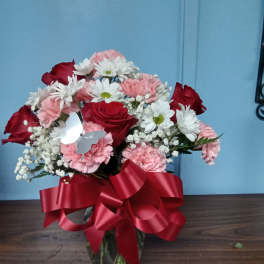 Bouquet of red roses, pink carnations, and white daisies in a glass vase with a red ribbon