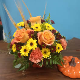 Orange roses and yellow daisies in a pumpkin vase with fall accents
