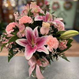 Pink lilies and carnations arranged in a glass vase with a pink ribbon.