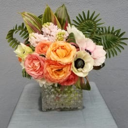 Mixed bouquet of peach, pink, and white flowers in a square glass vase